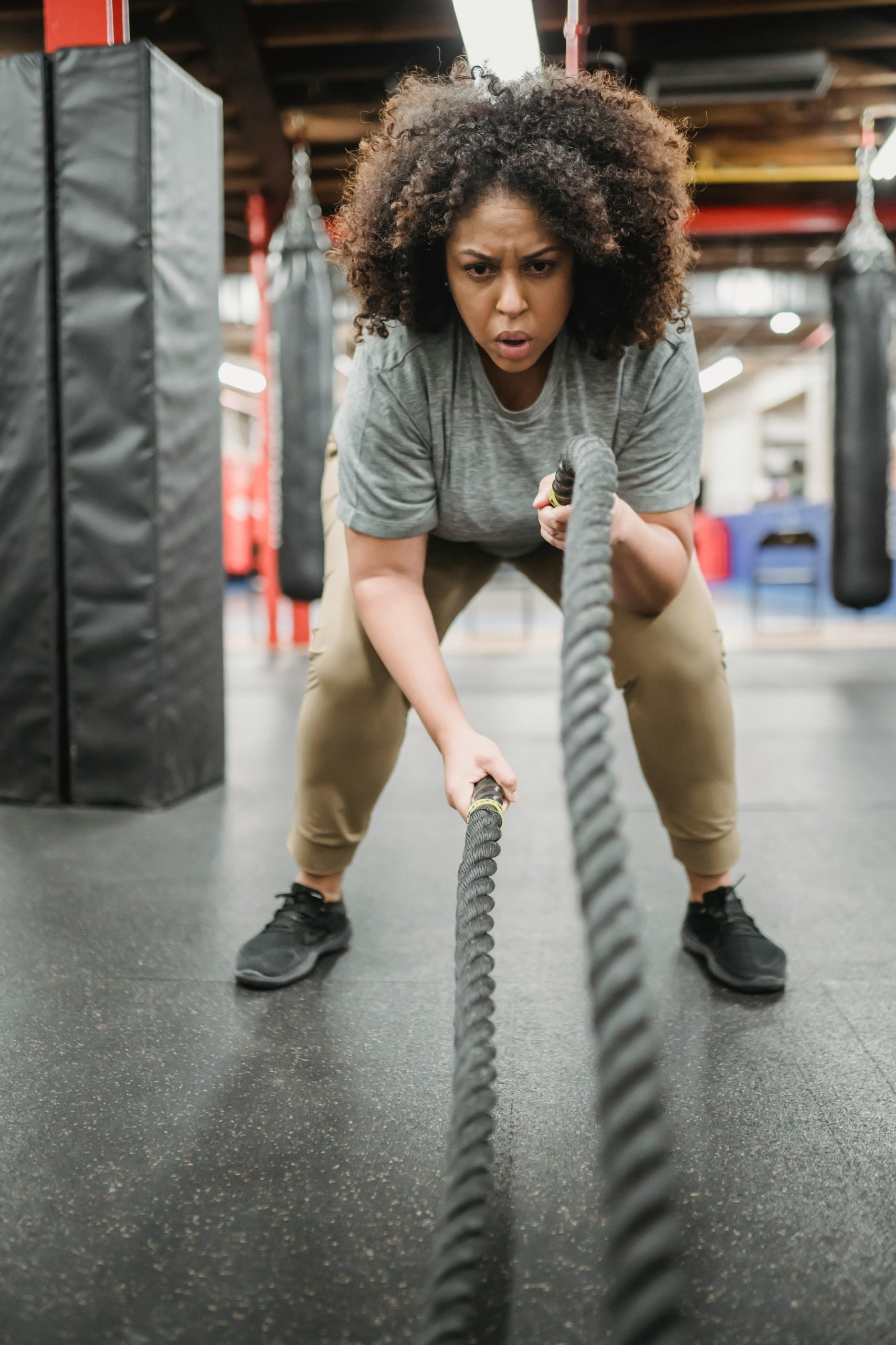 Focused woman working out with battle ropes in a gym, showcasing strength and determination.