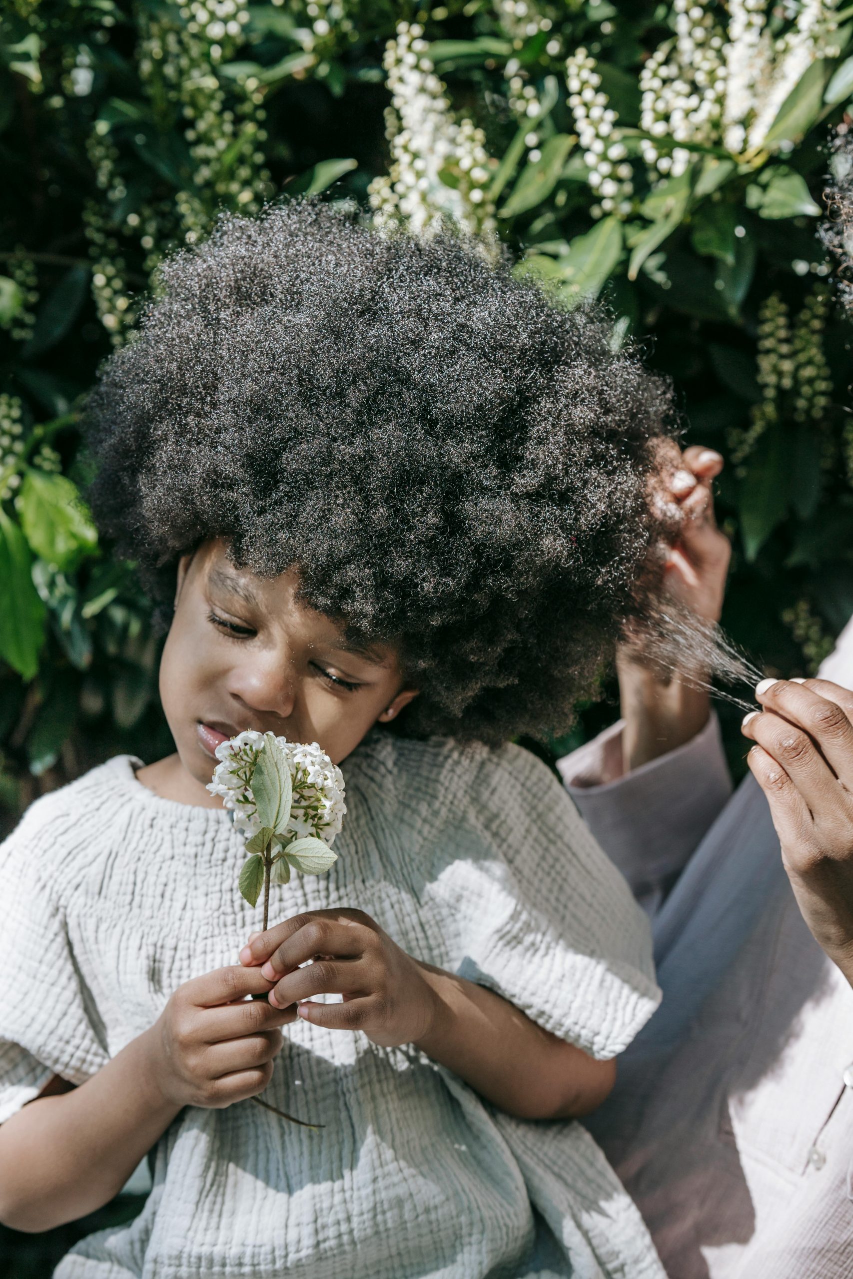 A young black girl holds a flower, enjoying a peaceful moment outdoors.